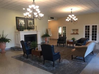 Elegant living room with fireplace, chandeliers, blue chairs, and beige sofa on a large rug