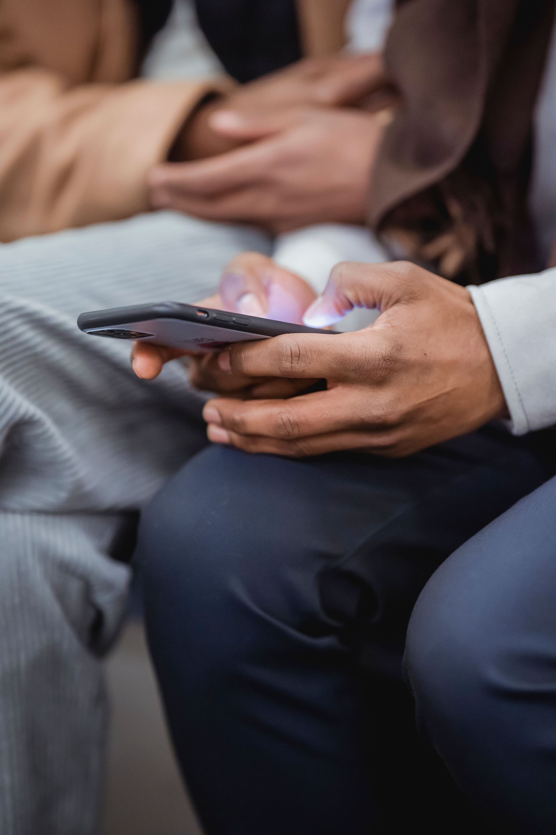 Hands holding a smartphone while seated, with blurred people in the background