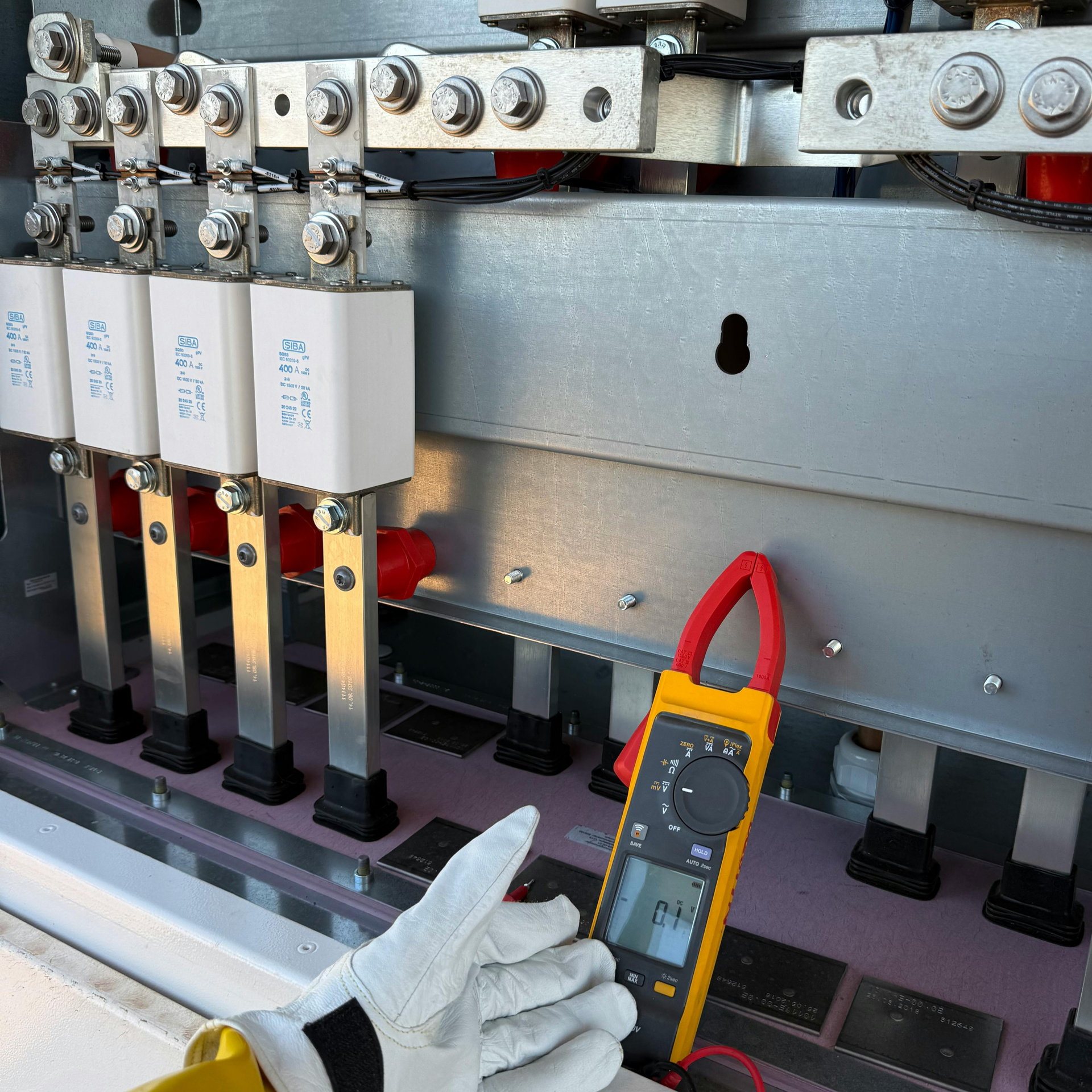 Gloved hand using a multimeter to test an electrical panel with labeled breakers and wiring