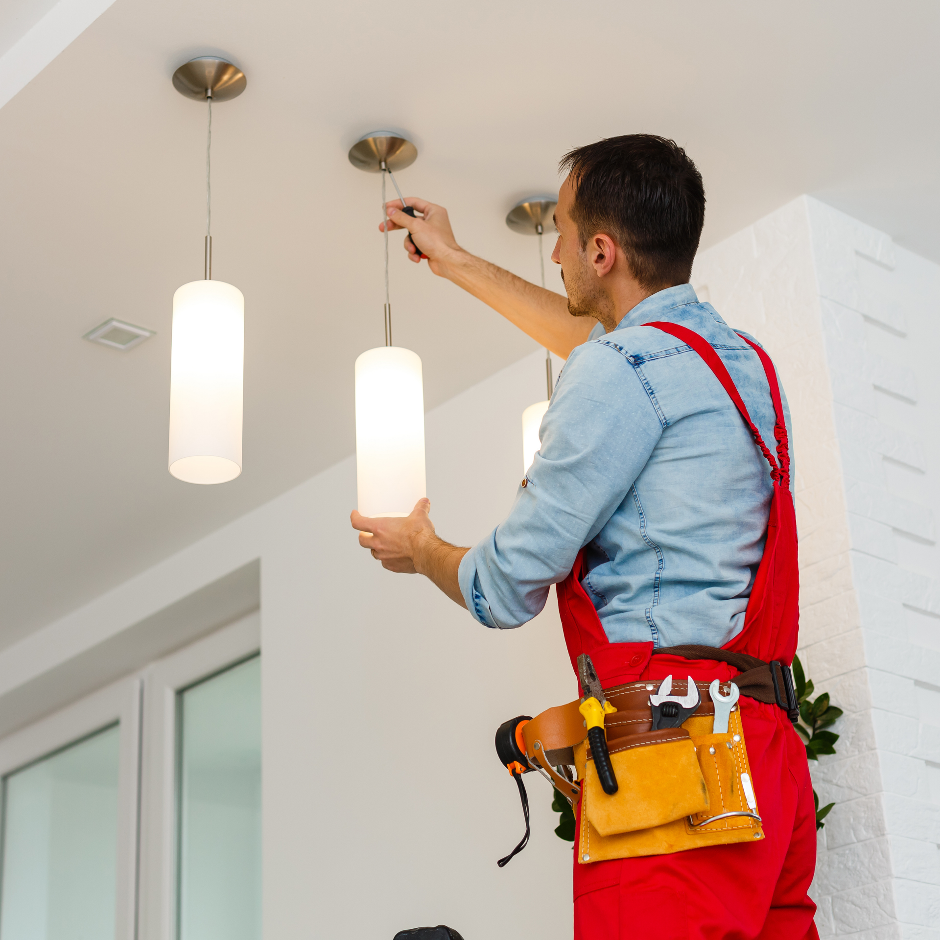 Electrician installing a white pendant light on a ceiling in a bright room