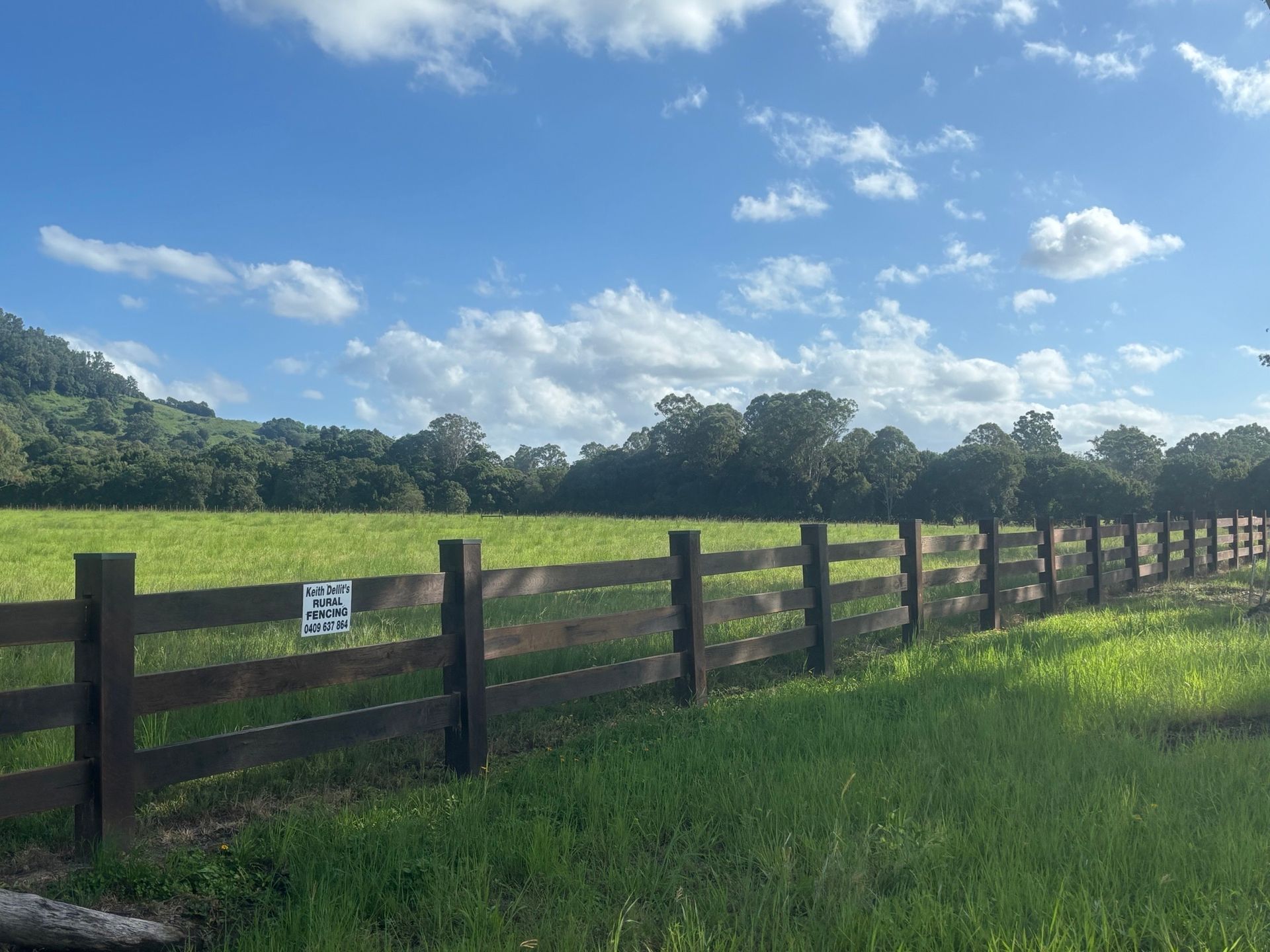 Green field with a wooden fence, trees, and blue sky with clouds. — Keith Dellit Rural Fencing in Yandina Creek, QLD