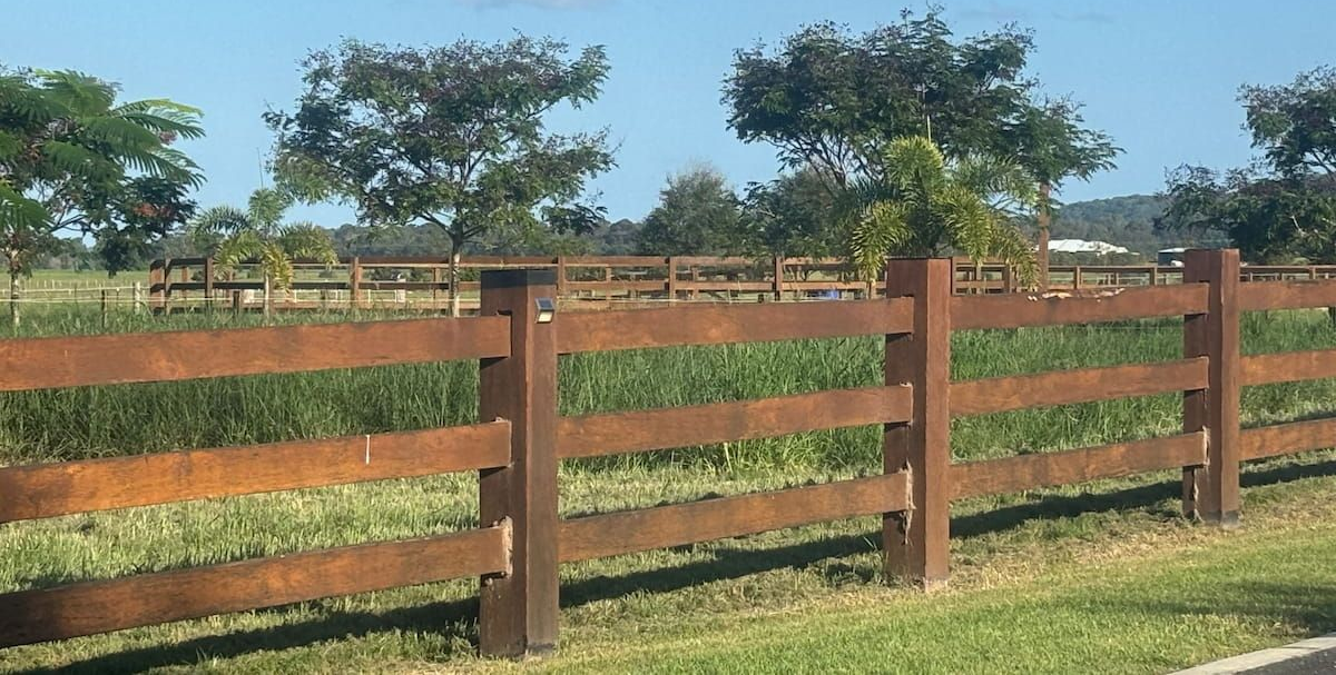 Rustic wooden fence in a field, with trees and blue sky in the background. — Keith Dellit Rural Fencing in Yandina Creek, QLD