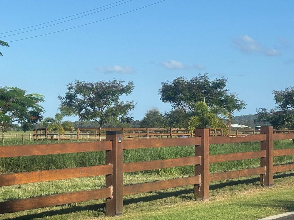 Wooden fence in a grassy field with trees and a blue sky. — Keith Dellit Rural Fencing in Yandina Creek, QLD