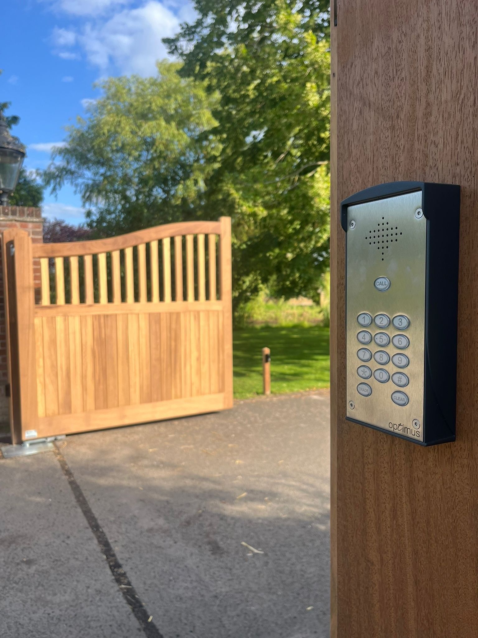 Gate intercom keypad on a wooden post beside an open driveway gate.