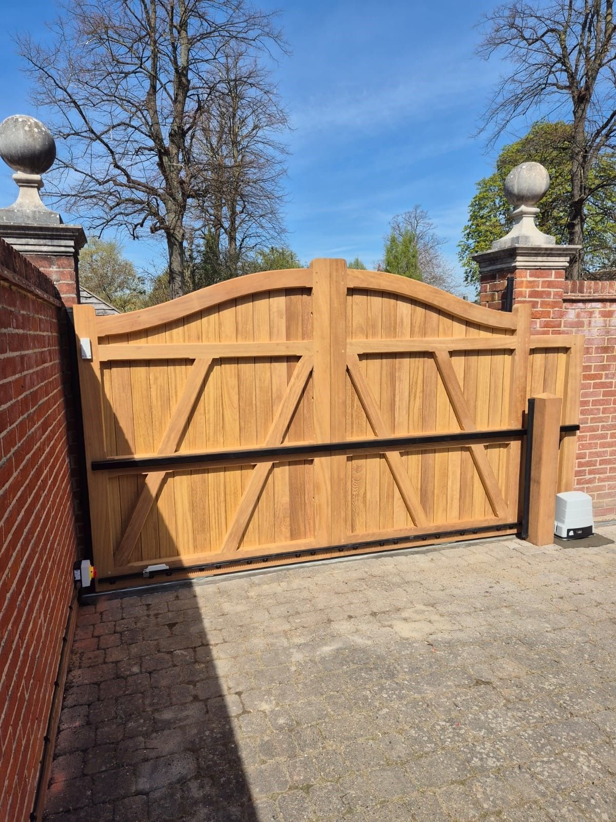 Wooden driveway gate between brick pillars under a blue sky