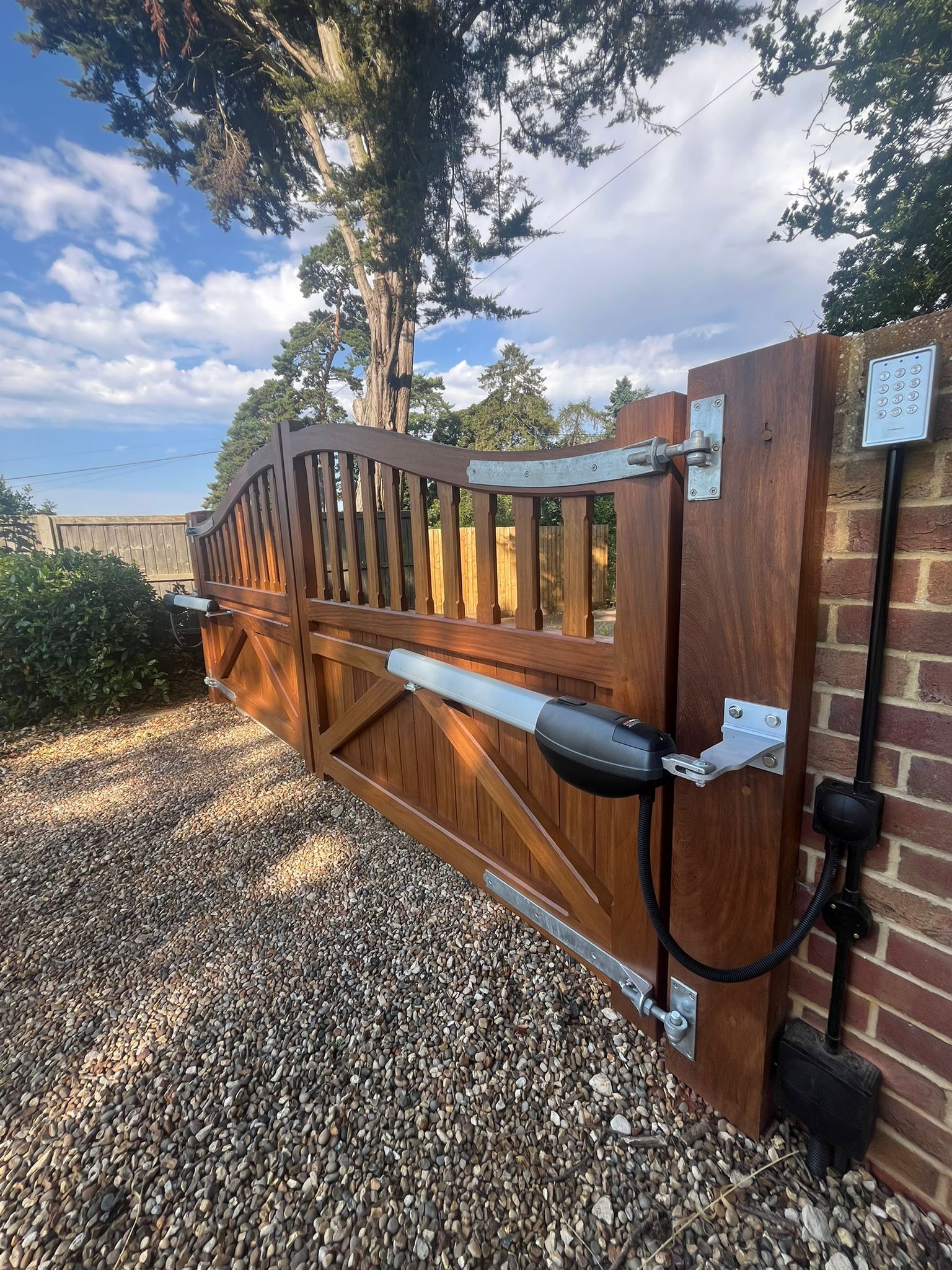 timber bespoke size cladded Electric Gate attached to brick columns with a large tree in the background