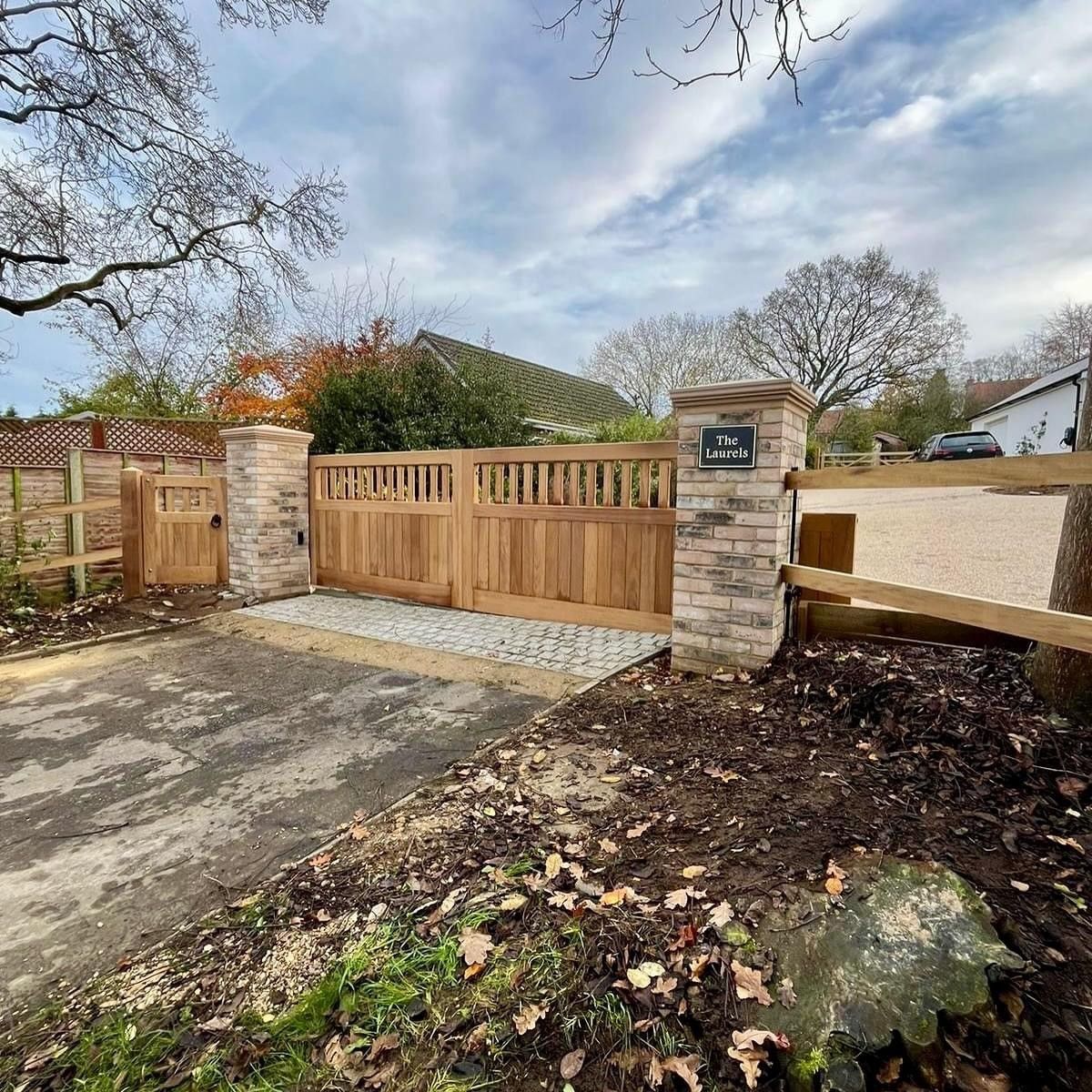 Wooden driveway gate between stone pillars beside a paved entrance and garden path