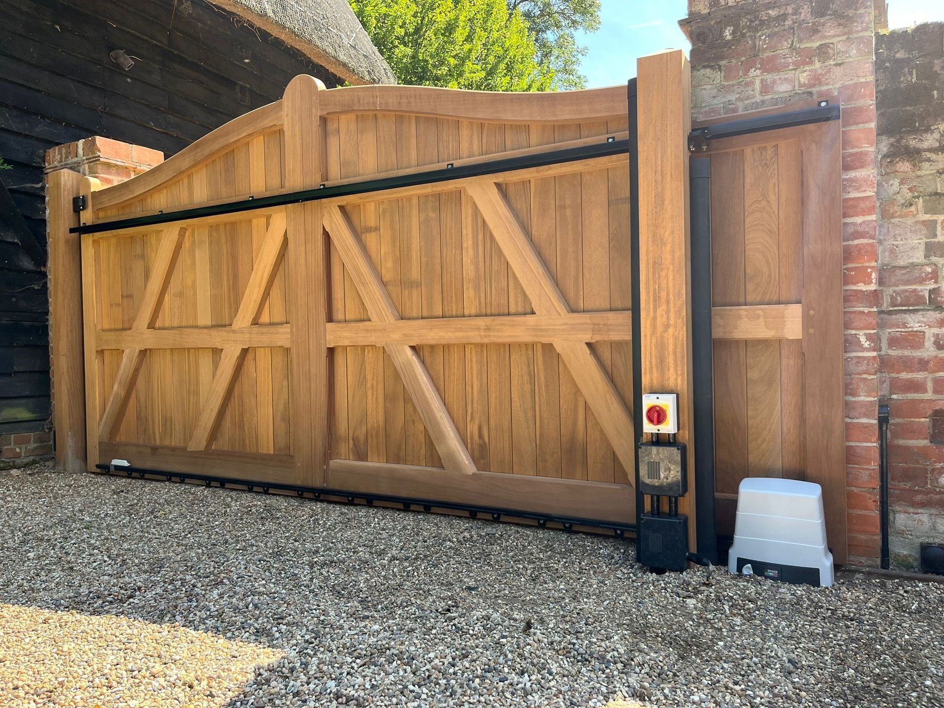 Wooden driveway gate with brick pillars and a keypad entry panel beside a gravel driveway.