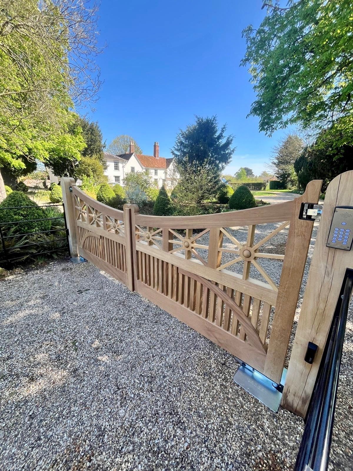 Wooden driveway electric gate on gravel entrance with white house and blue sky in the background