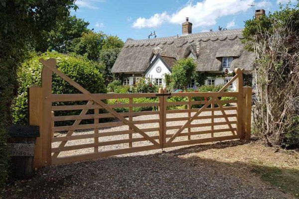 A wooden gate is leading to a thatched cottage.