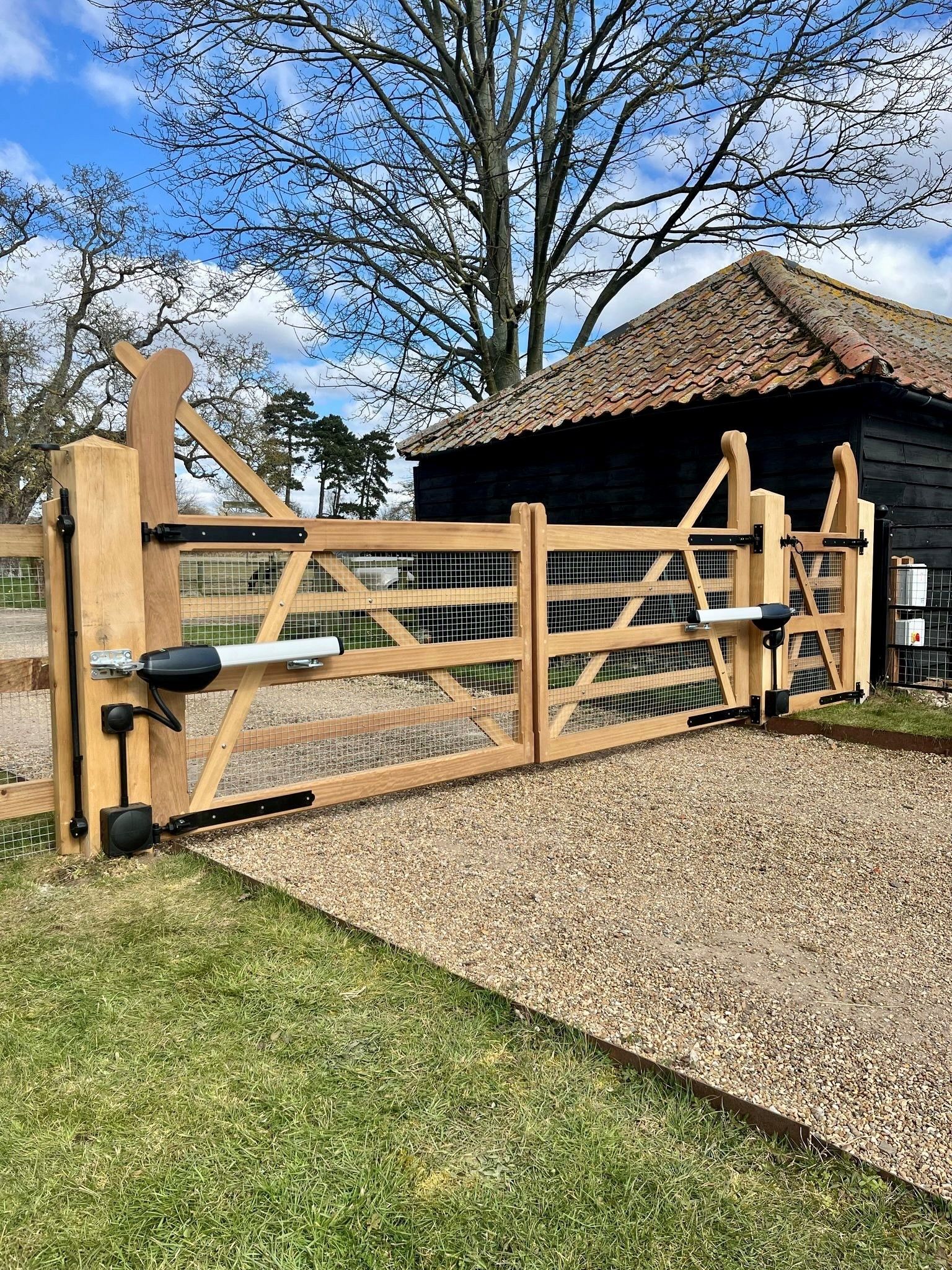 Bespoke Timber Electric gate that is farm gate style with an outbuilding next to it and a tree with no leaves and blue sky in the background 