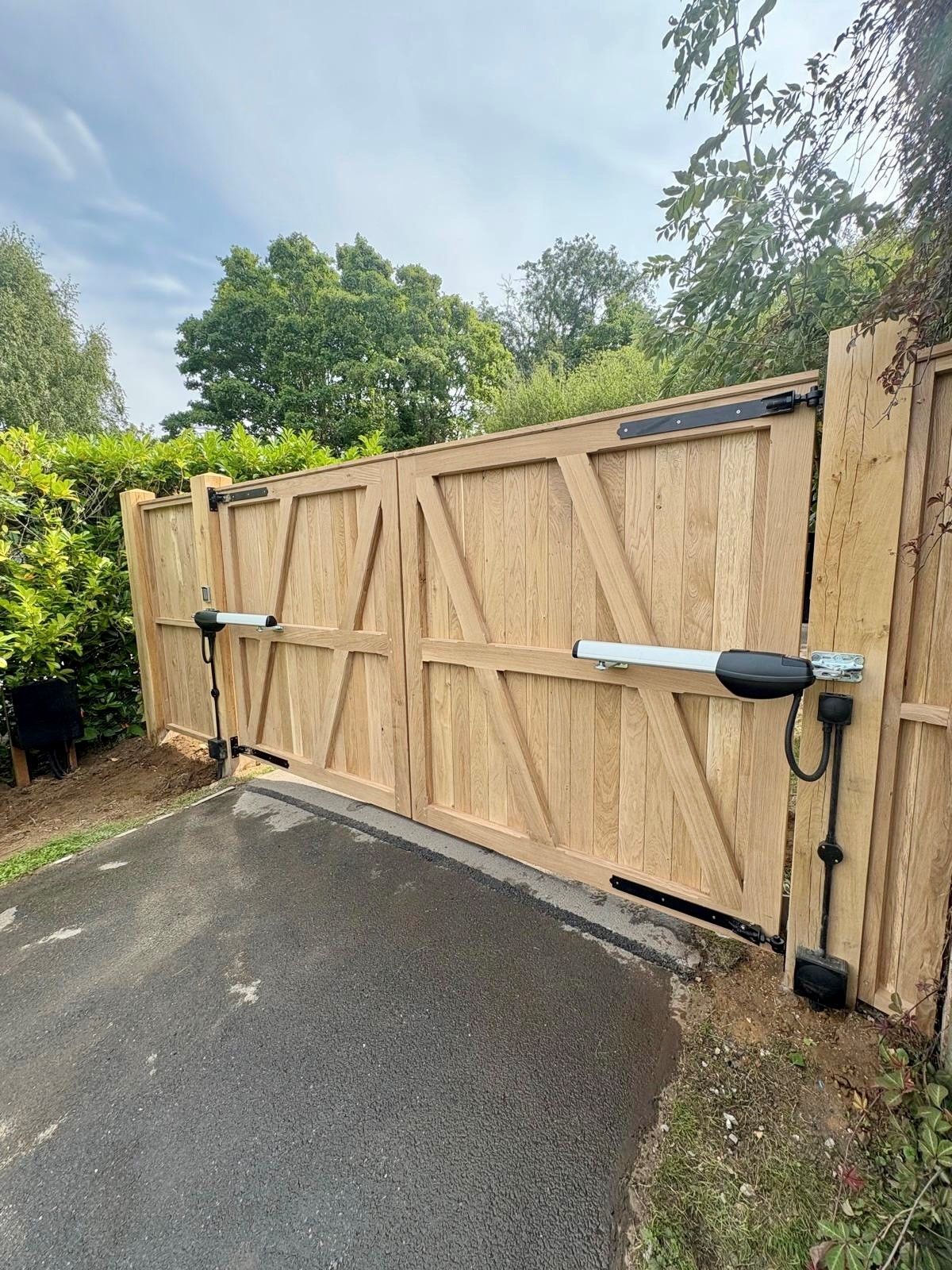 square bespoke timber Electric Gate with bushes either side of the door and blue skys in the background 
