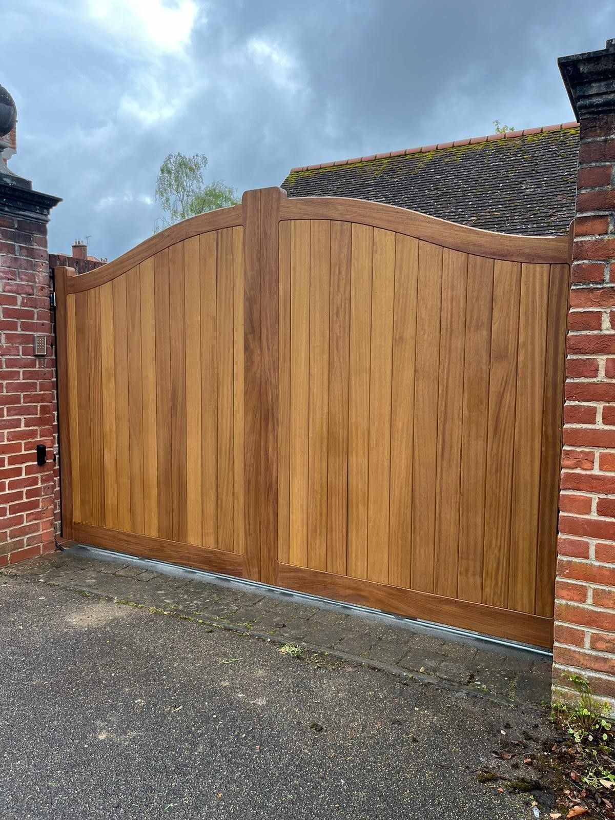 Wooden arched driveway gate between brick walls at the end of a paved driveway