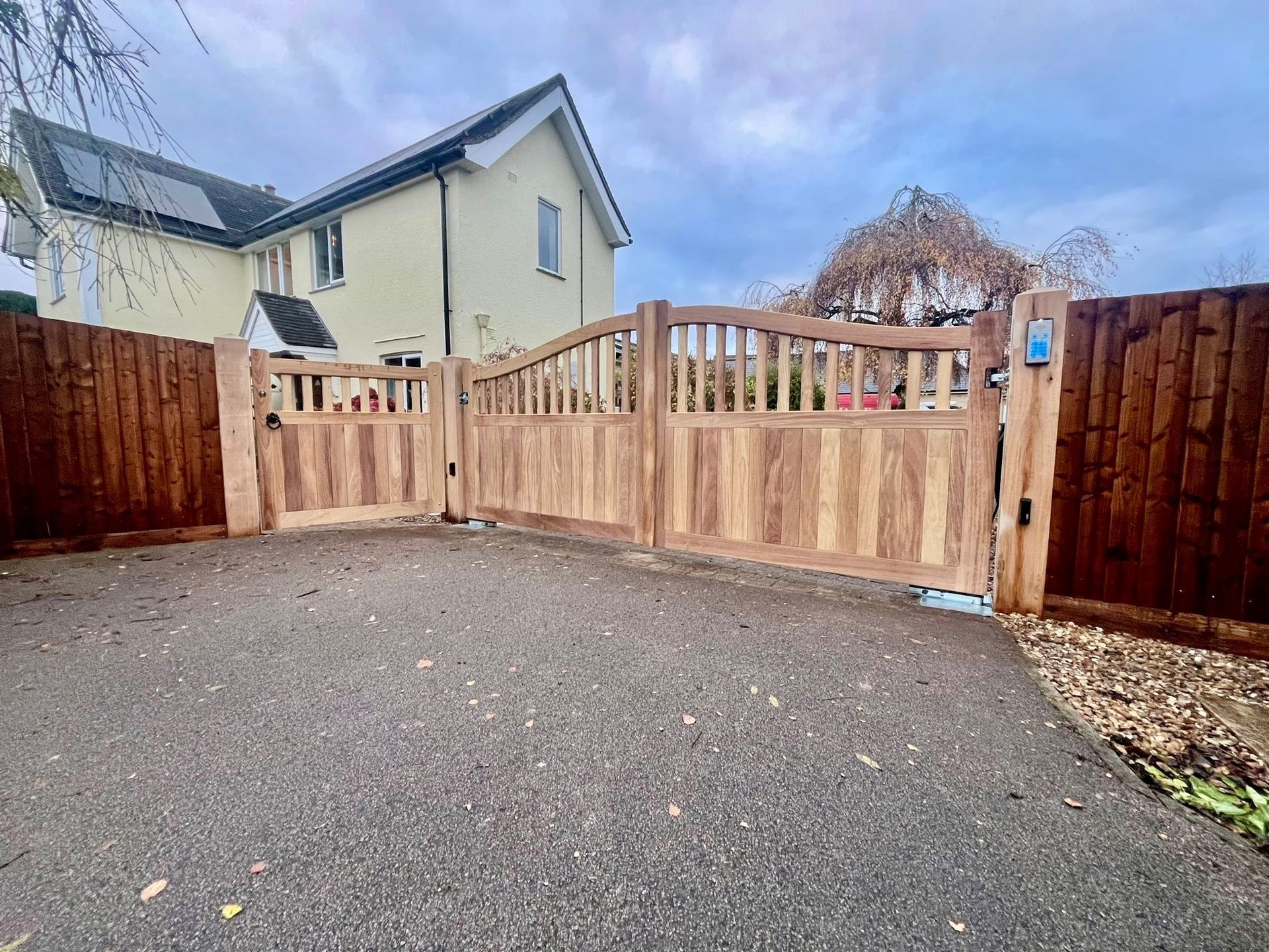 Wooden driveway electric gate and fence in front of a house on a cloudy day