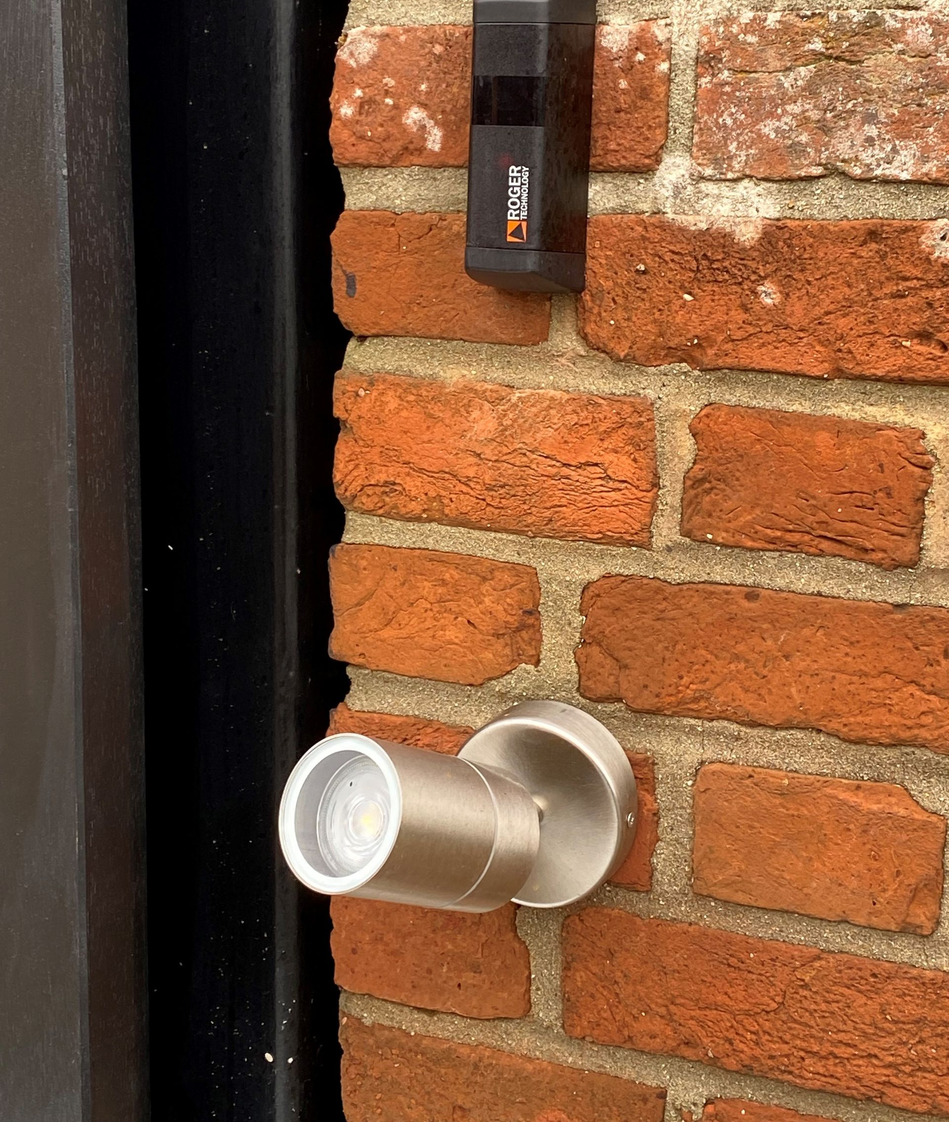 Silver wall-mounted security camera on a brick wall beside a black doorframe