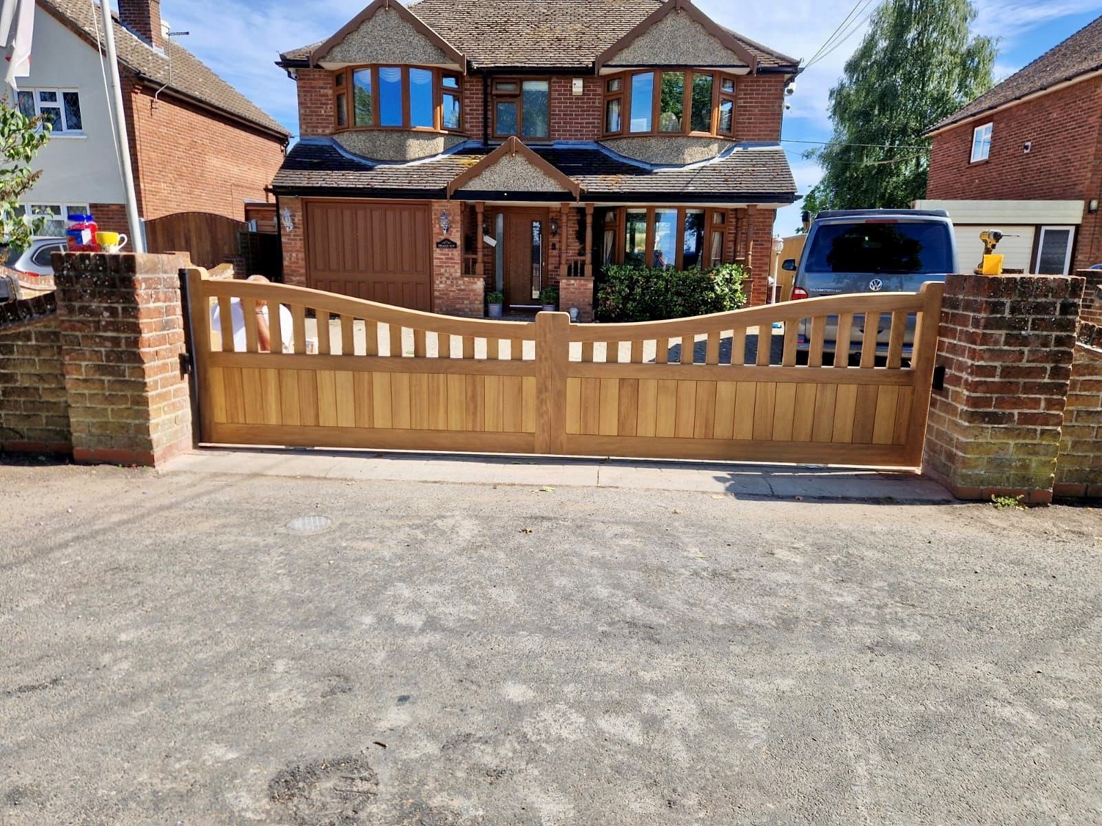 Wooden driveway electric gate in front of a brick suburban house with a parked car behind it