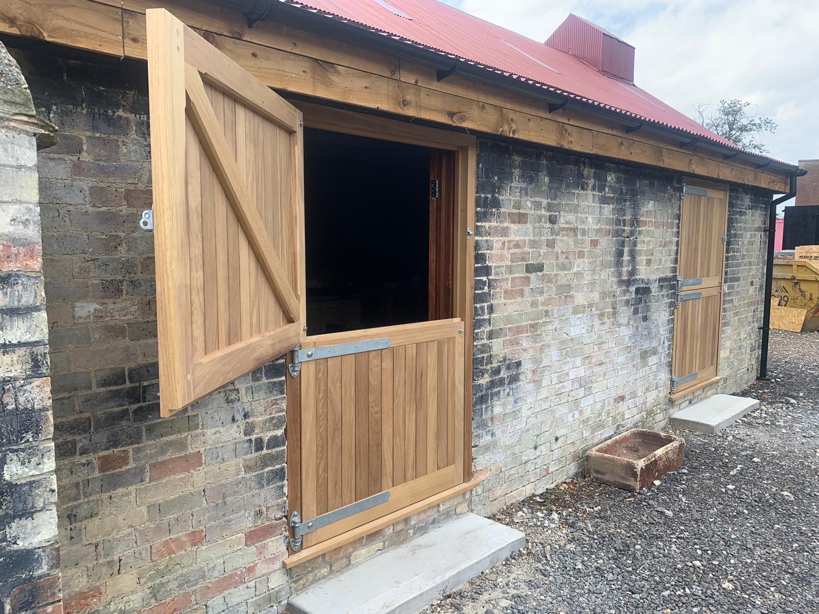 Rustic stone shed with open wooden door and small window under a red metal roof.