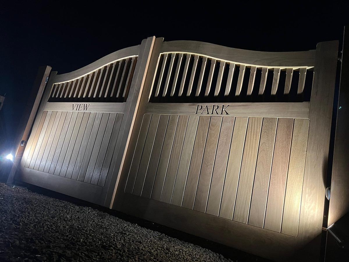 Illuminated metal electric gate at night with curved top and vertical slats