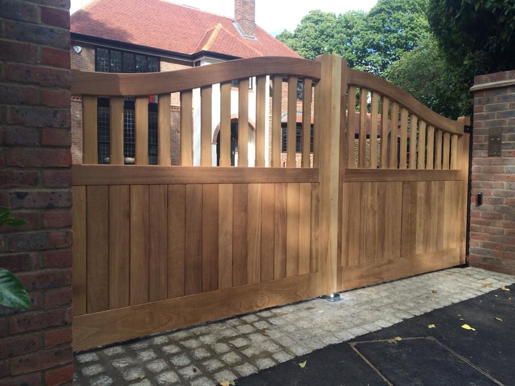 Wooden double driveway electric gate with curved slatted top between brick pillars and a paved driveway