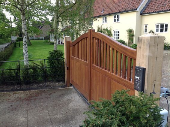 Wooden driveway electric gate with stone pillars beside a suburban house and garden path