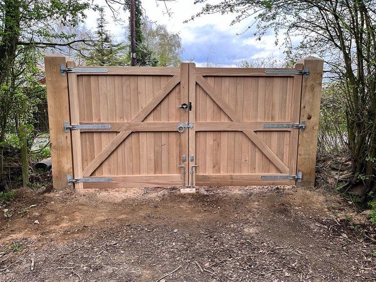 Wooden double gate with metal hinges in a wooded dirt driveway entrance