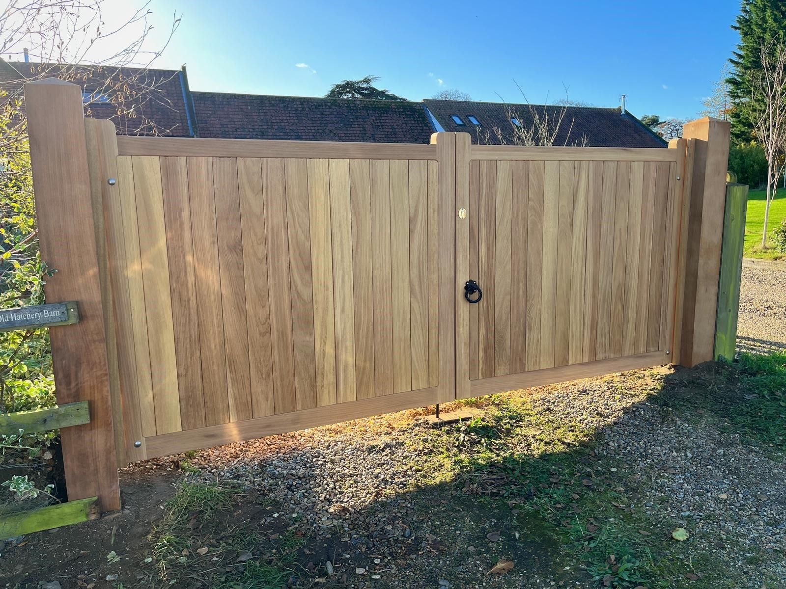Wooden driveway gate with a small latch, set between stone pillars in a sunny yard.