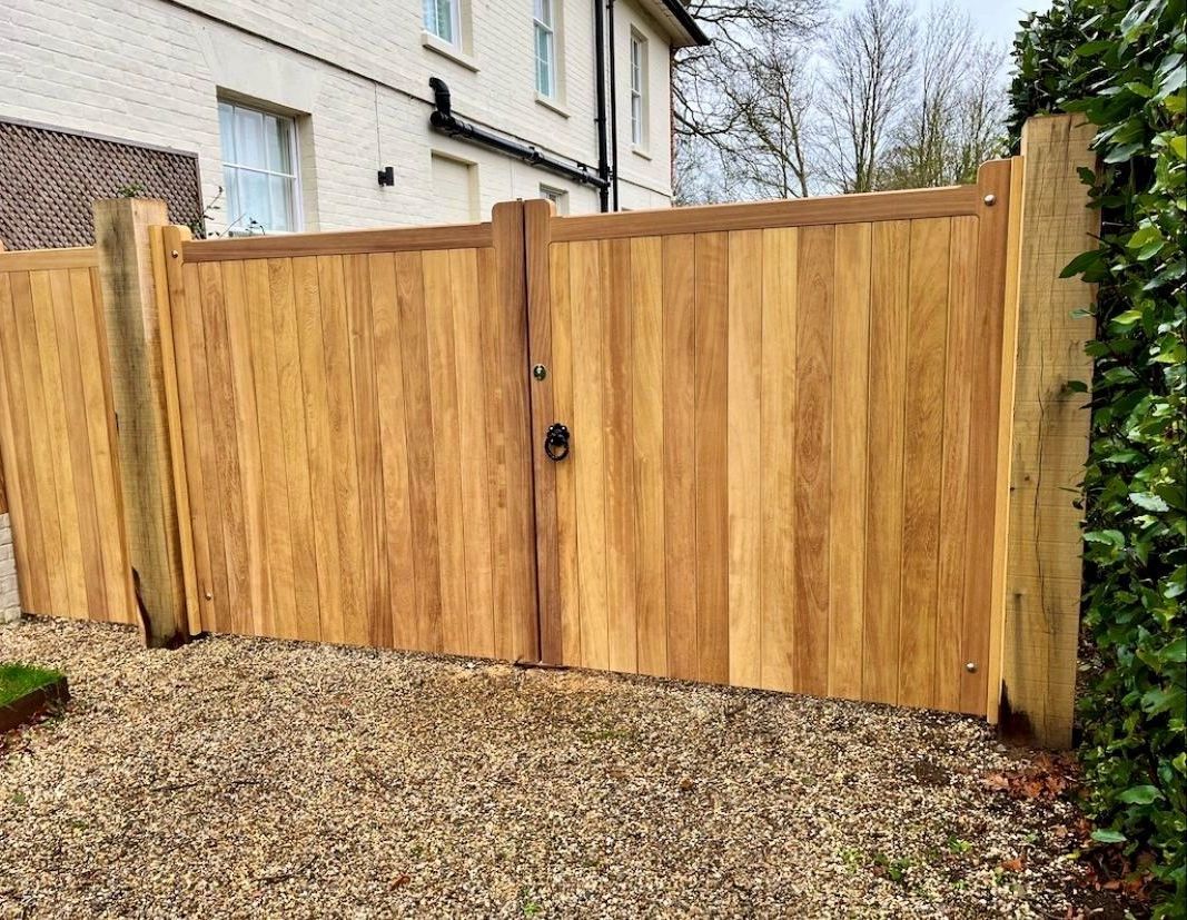 Wooden privacy gate and fence beside a house, with gravel path and greenery.