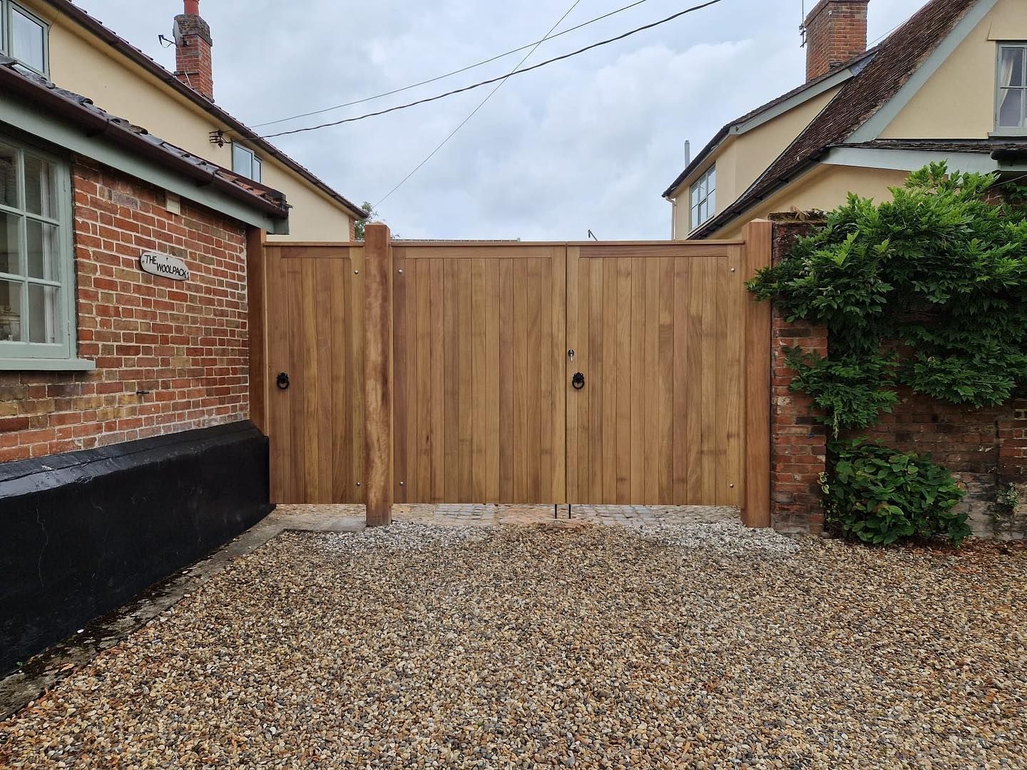 Wooden double gate between brick buildings with gravel driveway in front