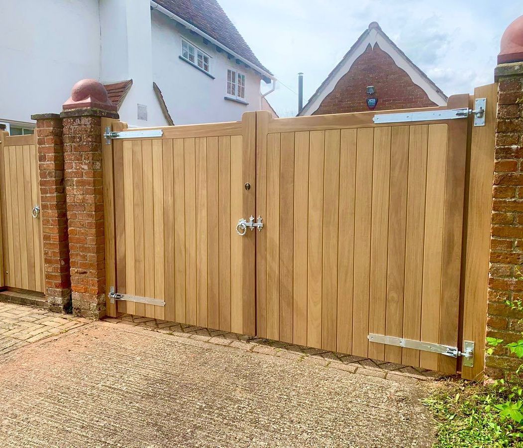 Wooden driveway gate beside a brick pillar and gravel driveway in front of houses