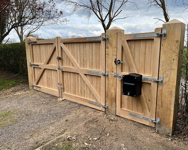 Wooden double gate with a black mailbox, set across a gravel driveway under leafless trees.