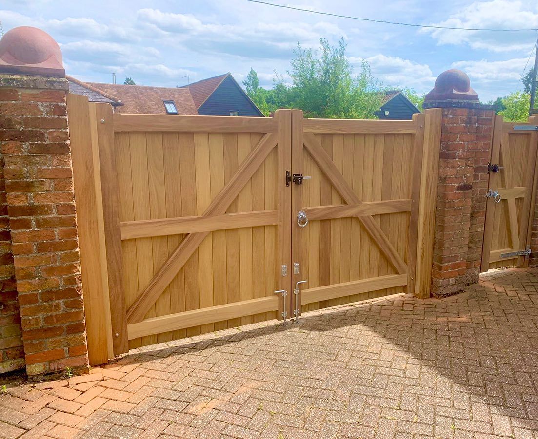 Wooden double driveway gate between brick pillars on a paved entrance under a blue sky