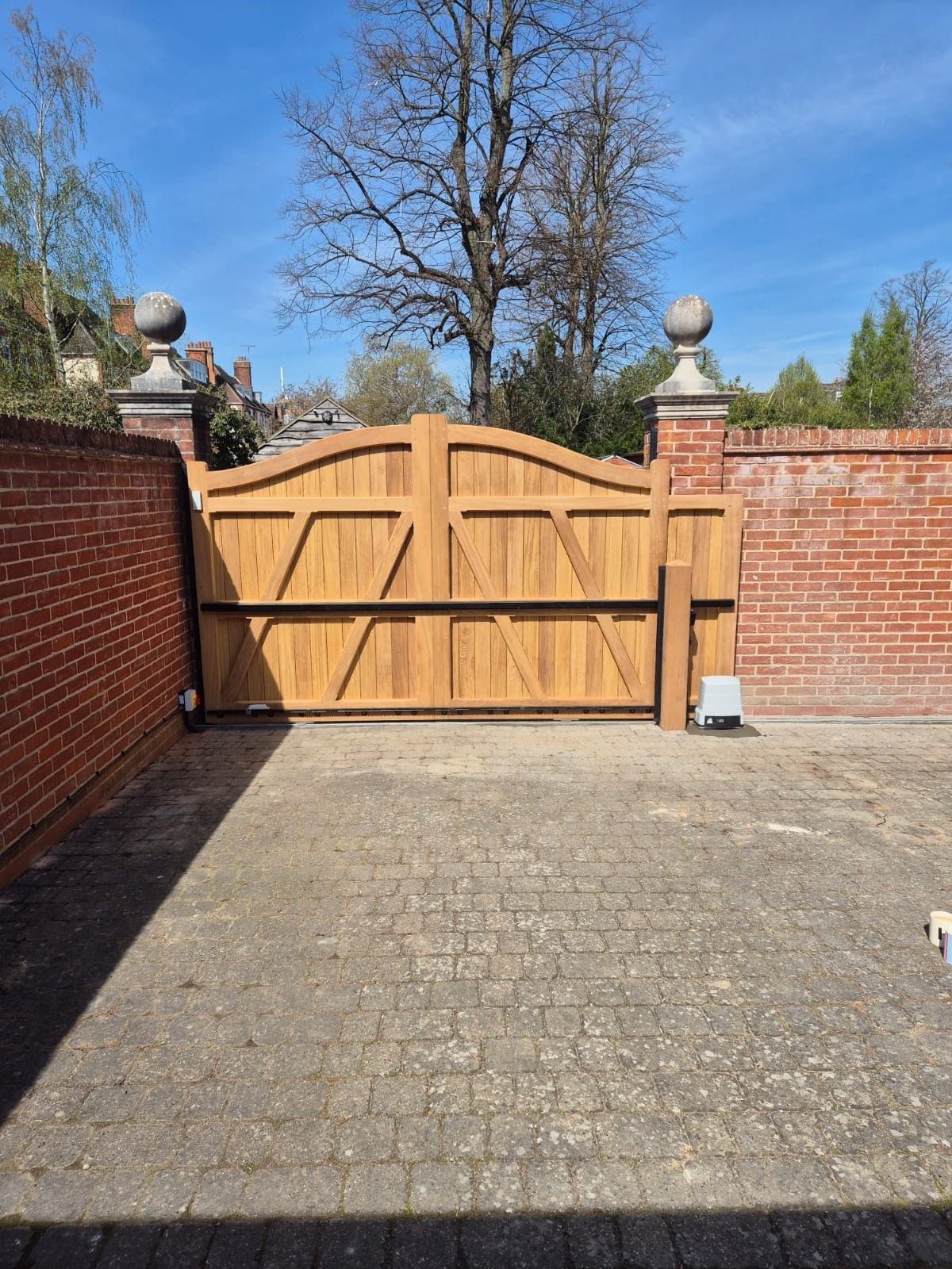 bespoke made timber Electric Gate with brick columns either side and blue sky in the background 