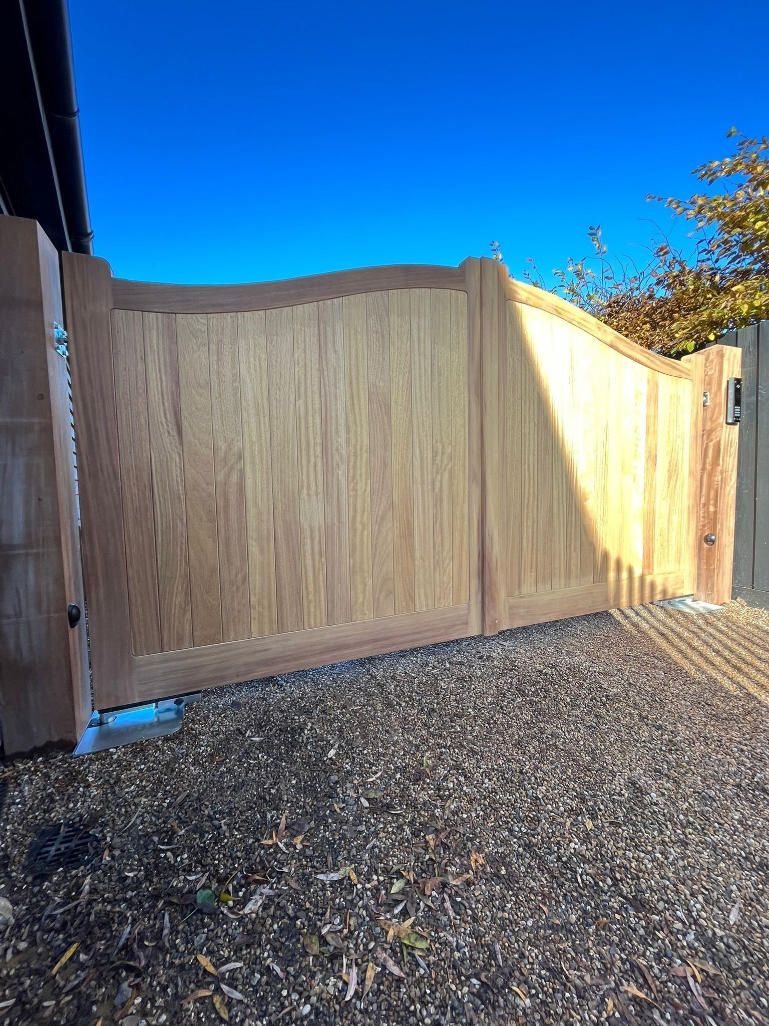 Wooden backyard fence and electric gate over gravel under a bright blue sky