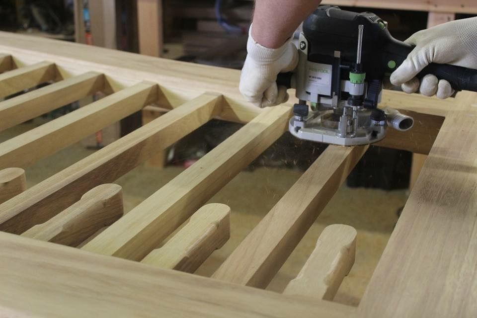 Gloved hands using a router to cut grooves in a wooden frame
