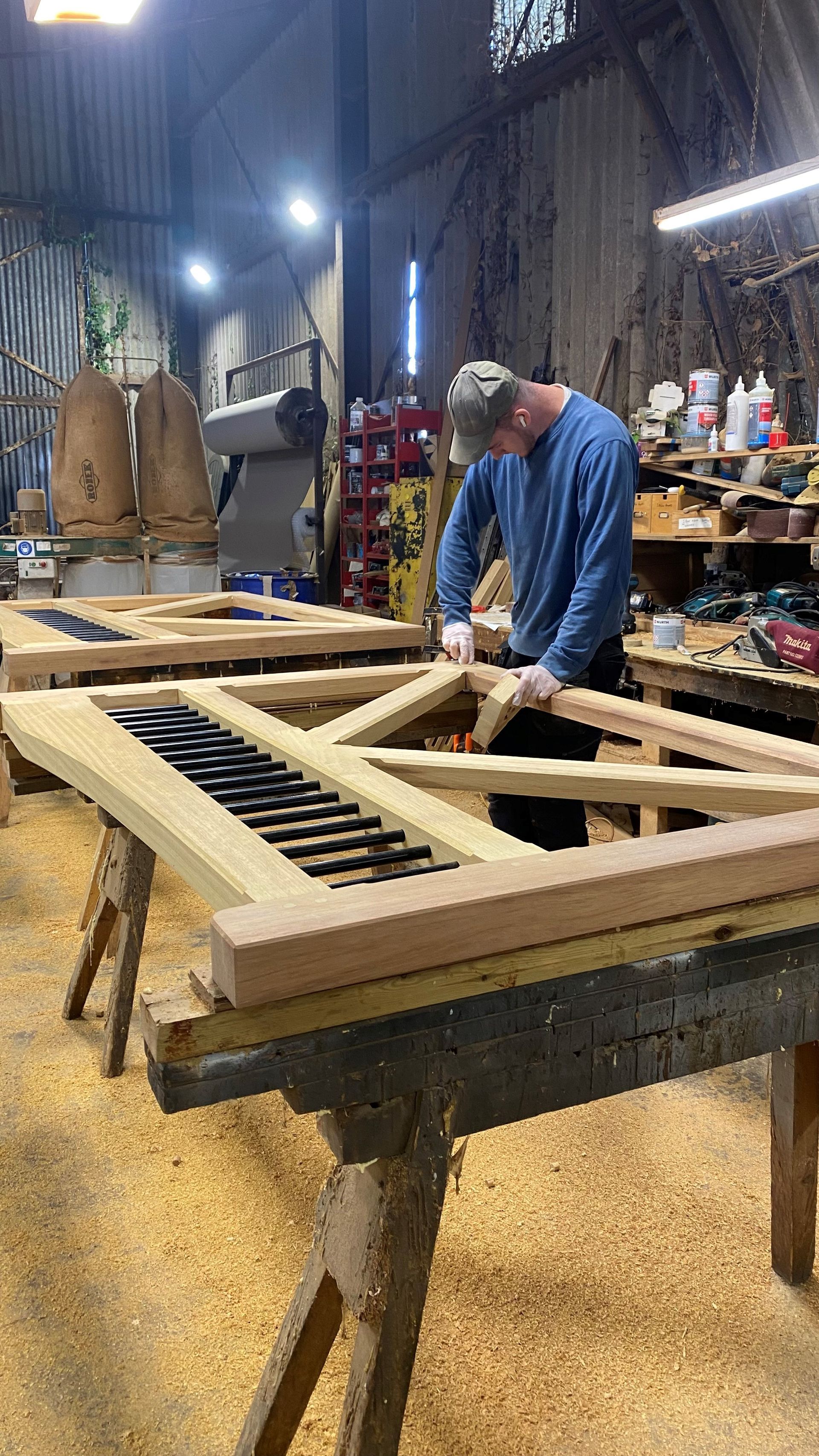 Person working on a large wooden frame at a workshop table with tools and shelves in the background