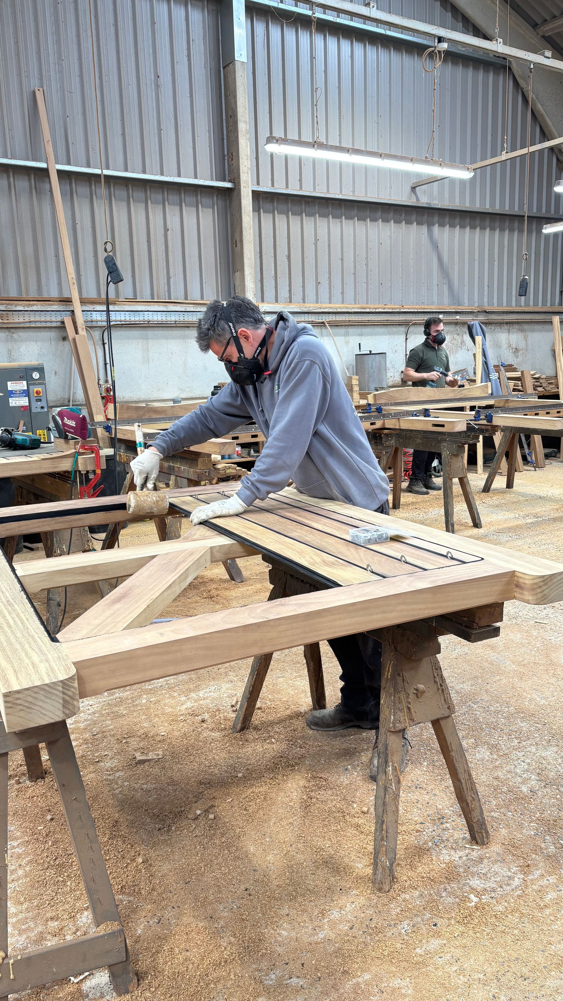 Workshop scene with a person sanding a wooden frame on sawhorses inside a large shed