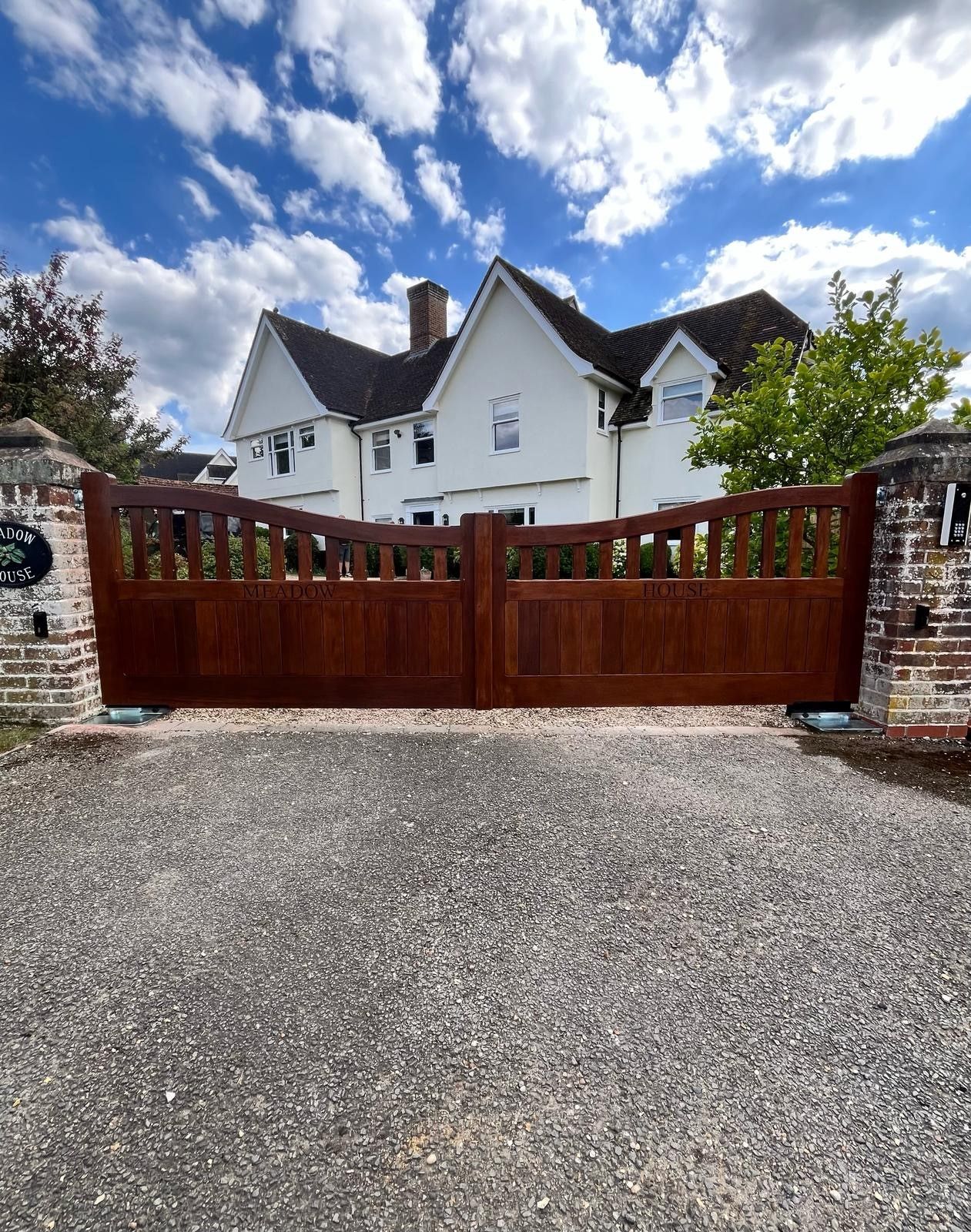 Wooden driveway gate before a white house under a bright blue sky with clouds