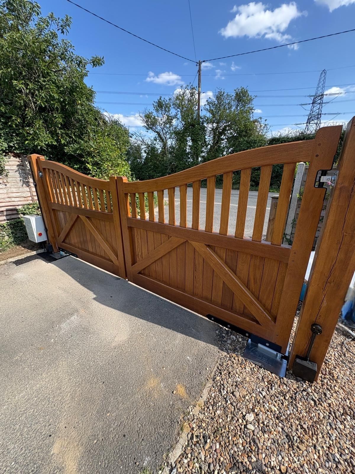 Wooden driveway gate beside a gravel path under a sunny blue sky