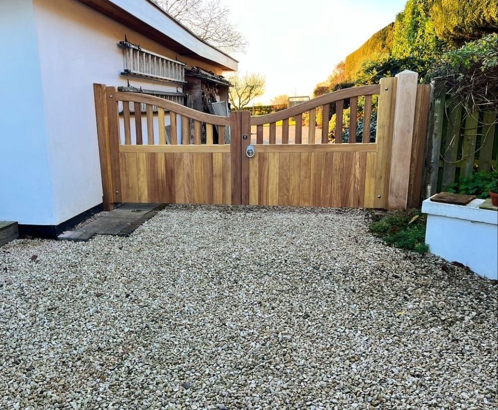 Wooden driveway gate with gravel courtyard, white house wall, and green hillside in the background