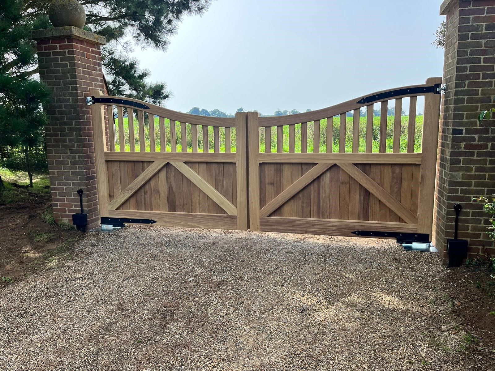 Wooden double driveway gate with brick pillars and gravel foreground, set against a cloudy sky