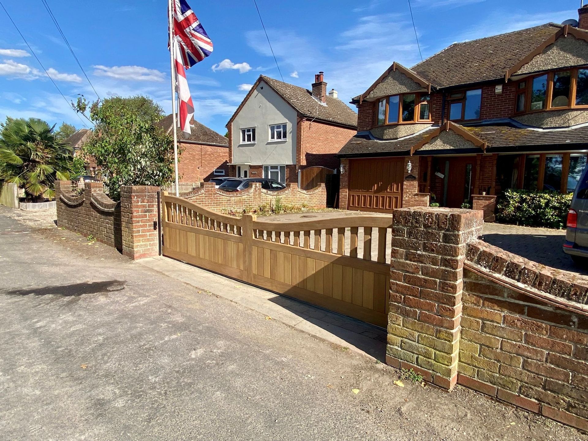 Brick house with a wooden gate and Union Jack flag beside a quiet driveway under a blue sky
