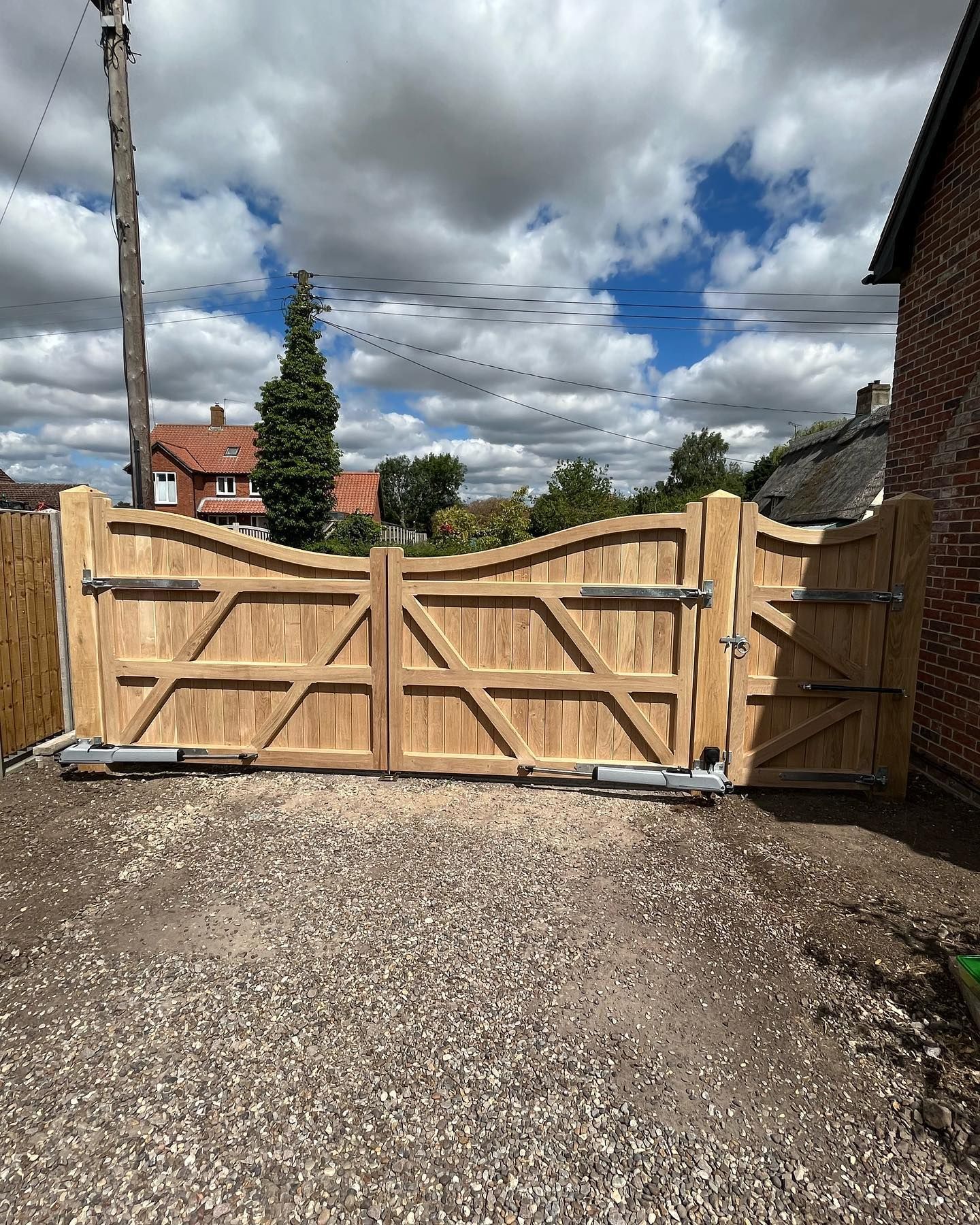 Wooden double driveway gate between brick walls and fencing under a cloudy sky
