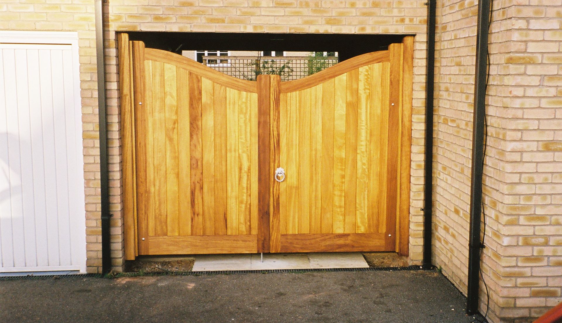 Wooden double driveway gate set between brick walls and a white garage door.