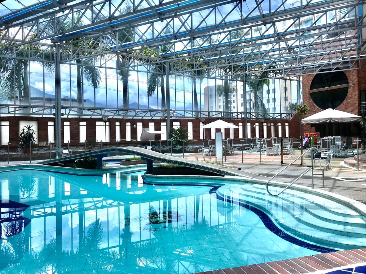 Una gran piscina cubierta con techo de cristal rodeada de palmeras.