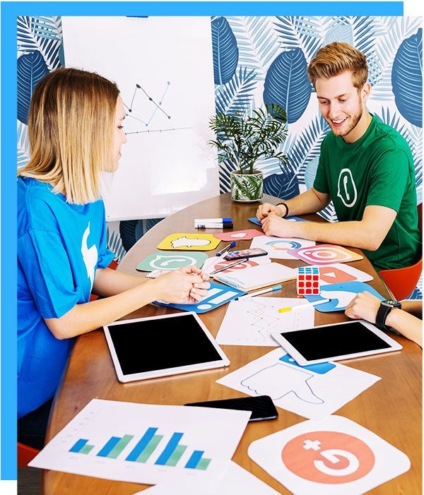 Happy people working around a table covered with icons, pages, tablets, pens  and a Rubik's cube