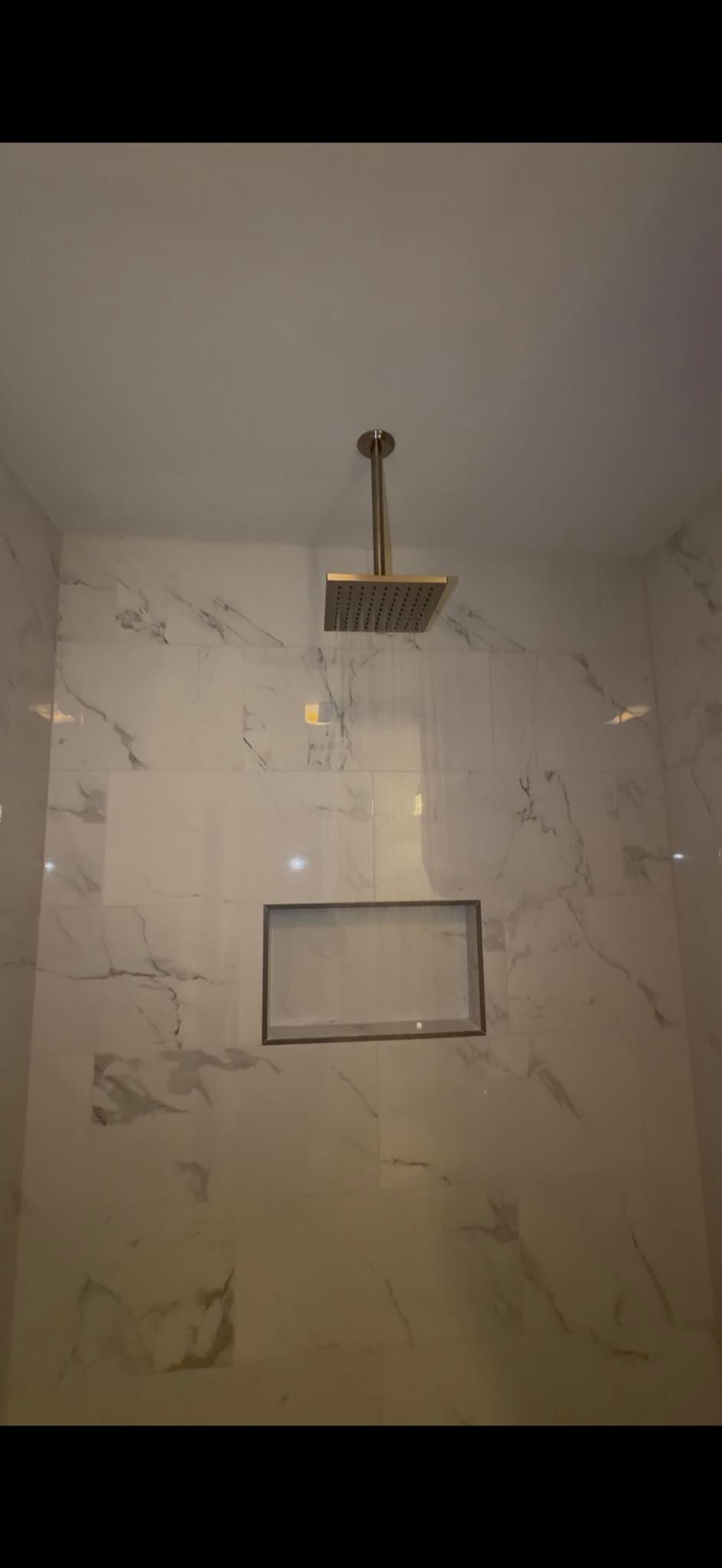 Shower with marble walls, recessed shelf, and gold rain shower head.