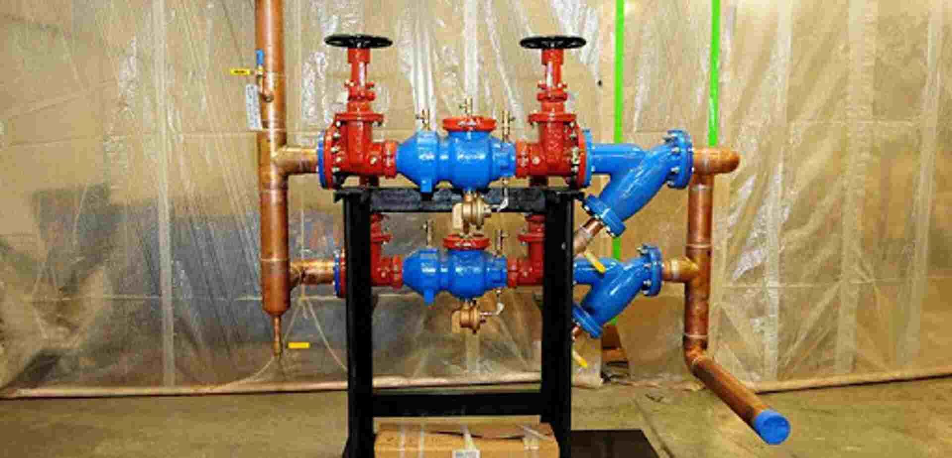 Pipes with valves and filters; red, blue and copper; installed on a black metal frame.
