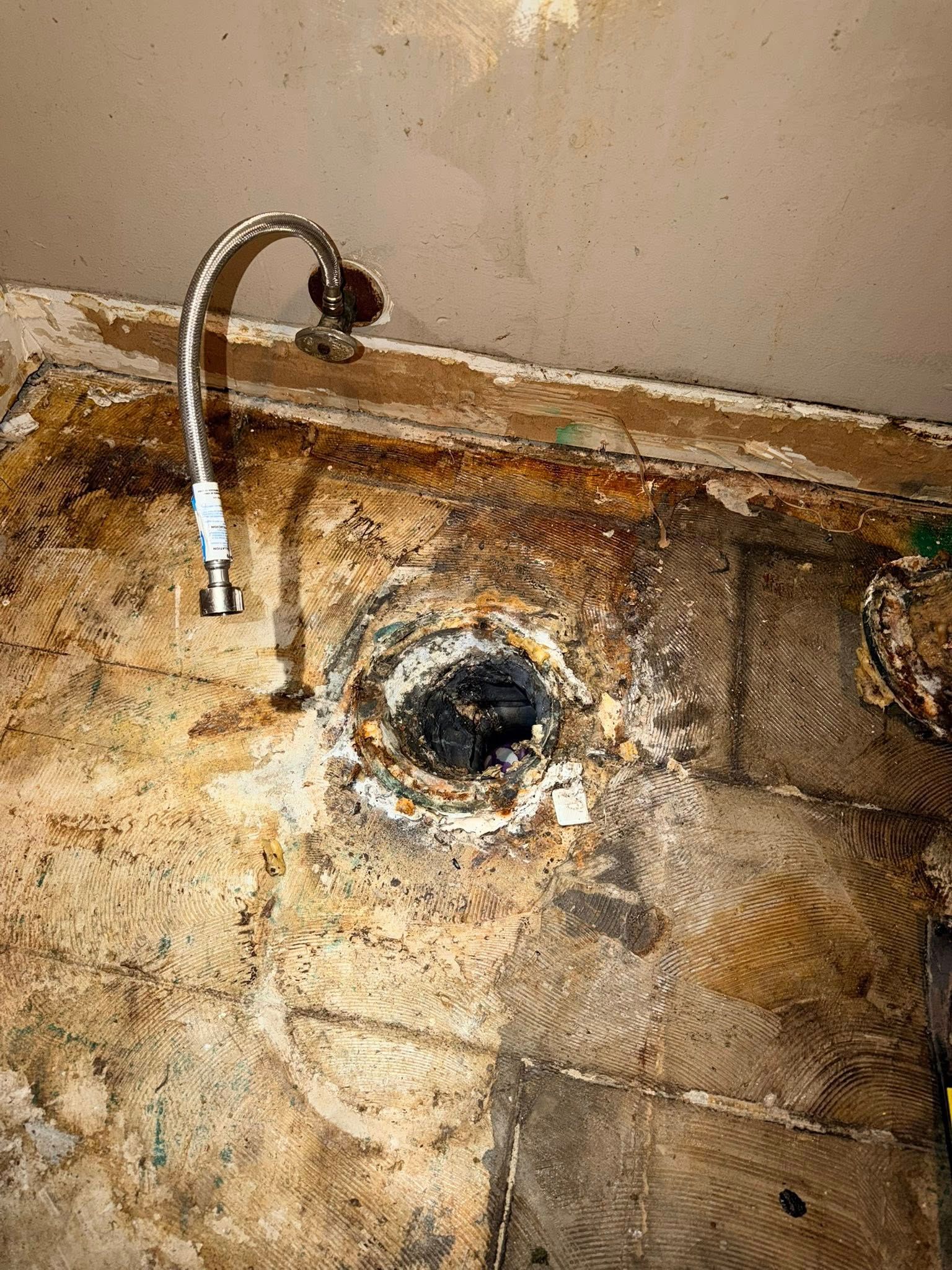 A hole in damaged wood with a metal faucet and water line attached above.