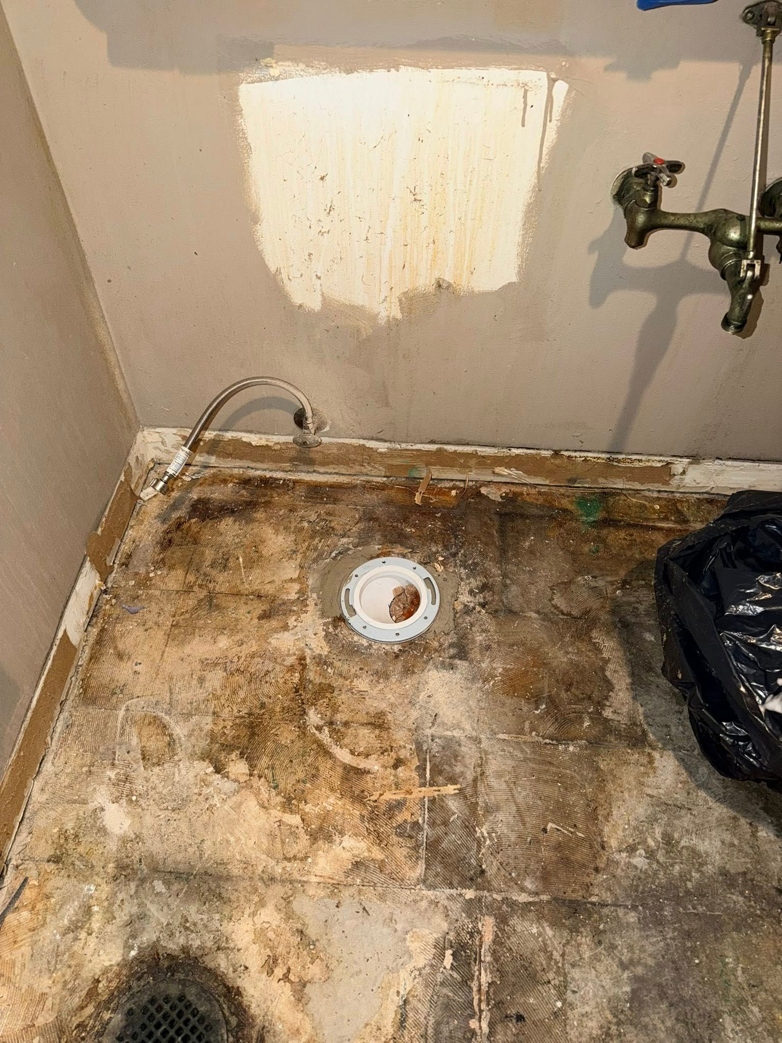 Damaged bathroom floor with exposed plumbing, stained walls, and fixture.