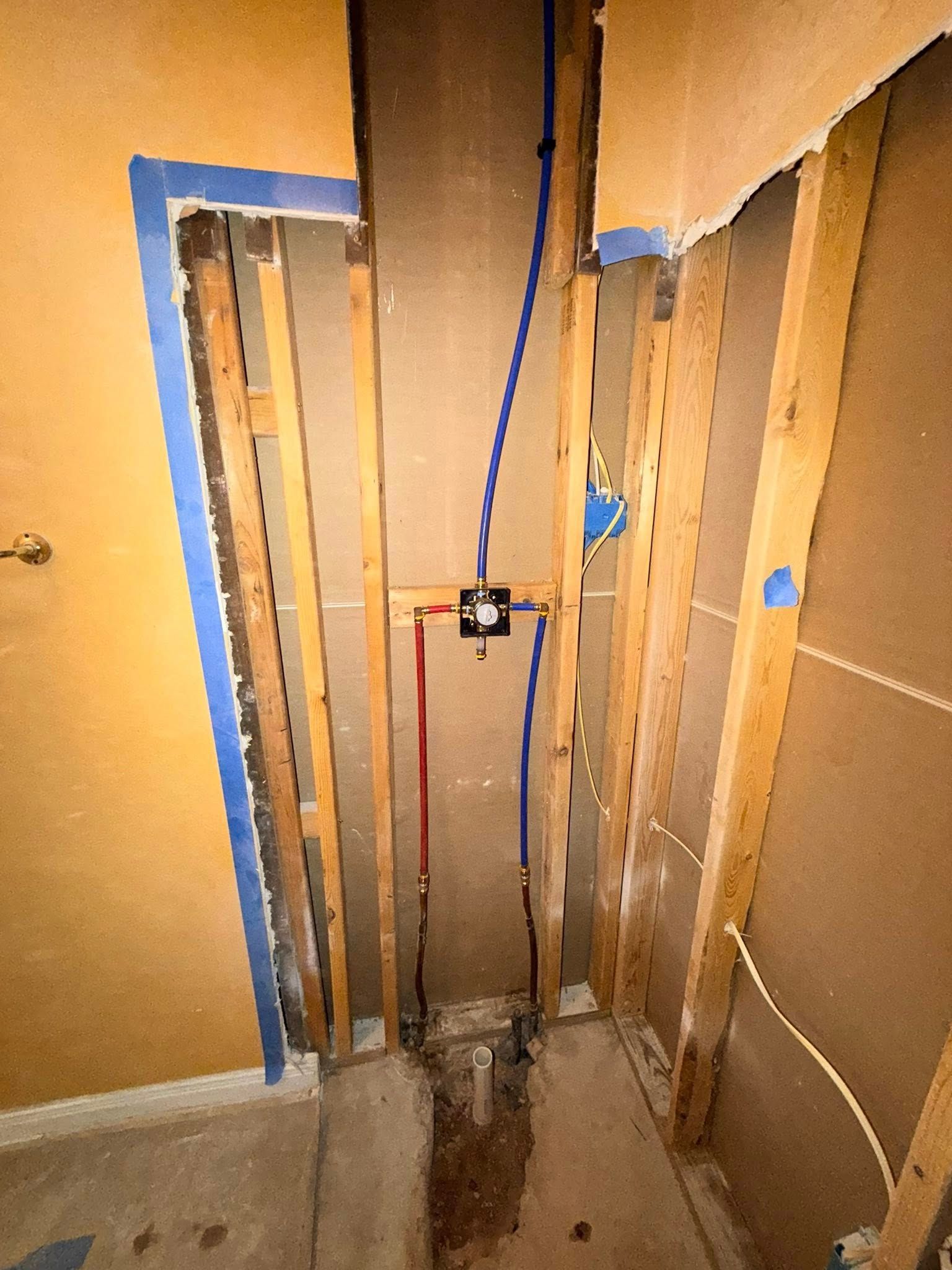 Bathroom remodel: exposed plumbing and framing, blue water lines, red hot water line, unfinished walls.